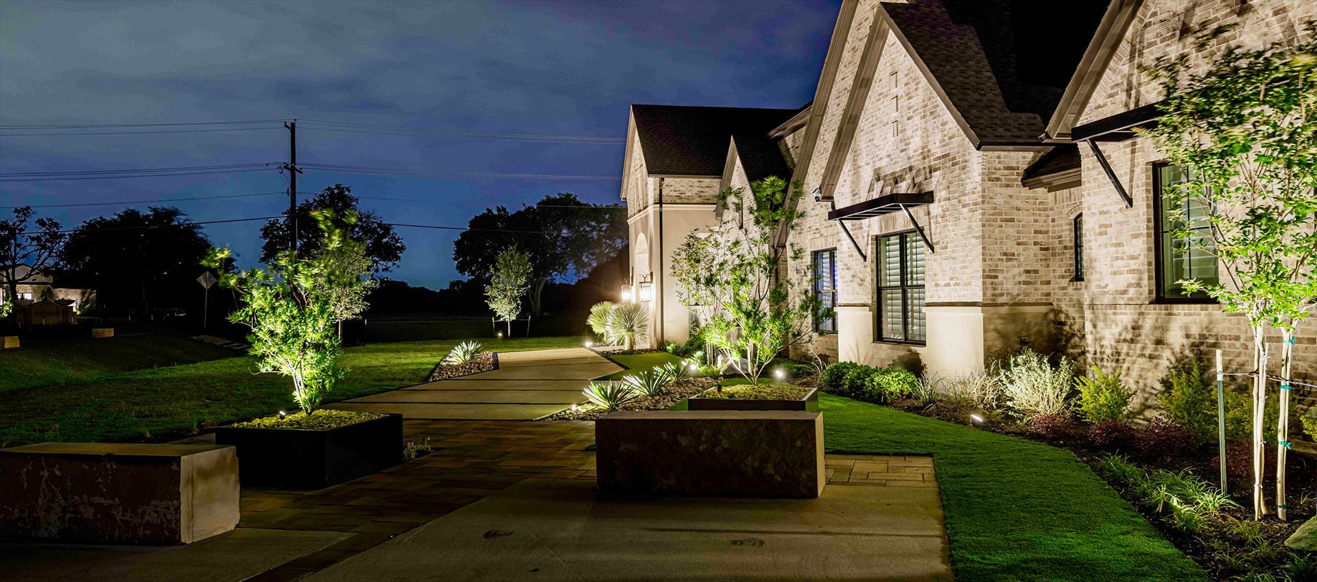 Stone estate at night with roofline Christmas lights, wreaths and uplit trees