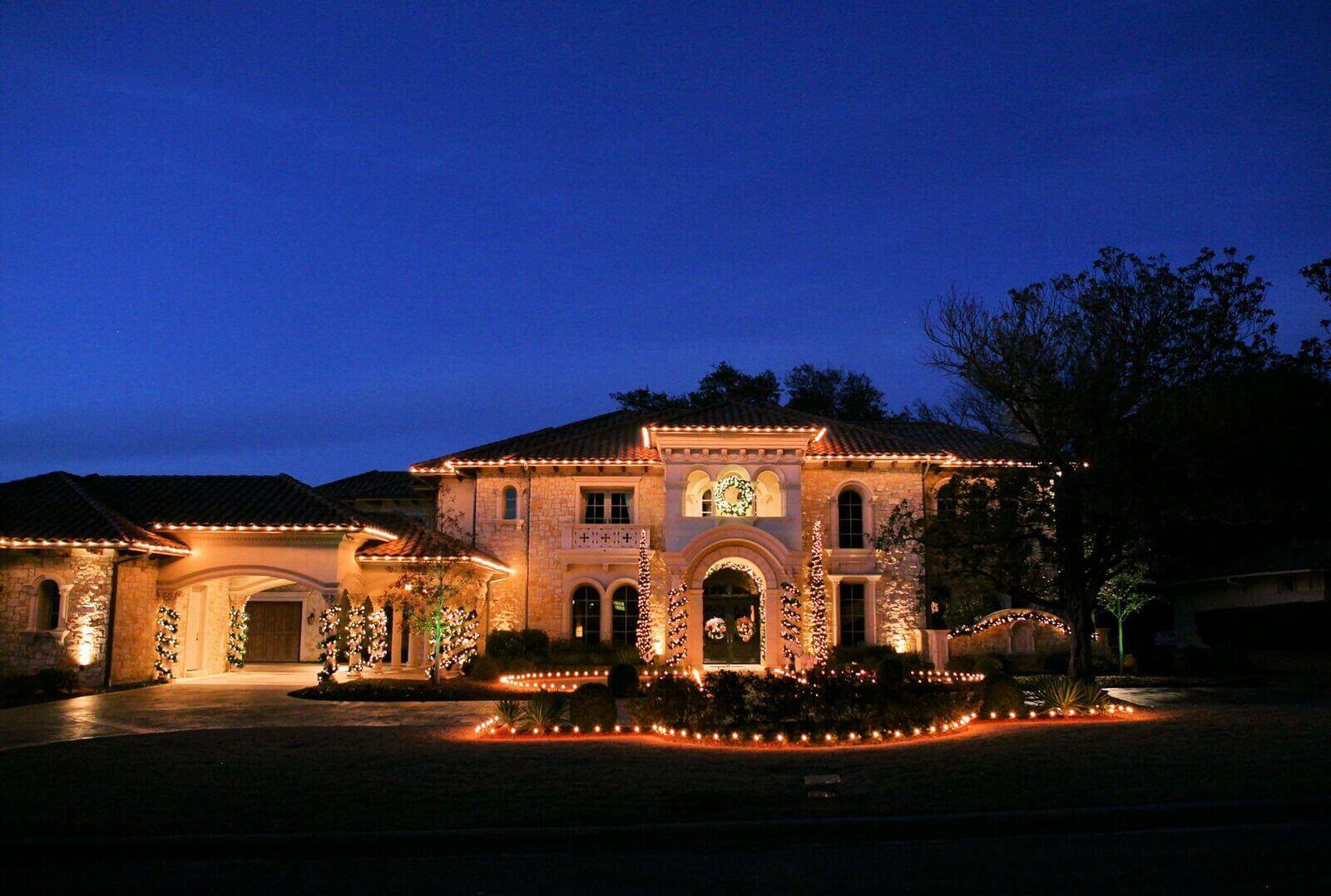 Home with warm white lights outlining the eaves against a deep blue dusk sky.