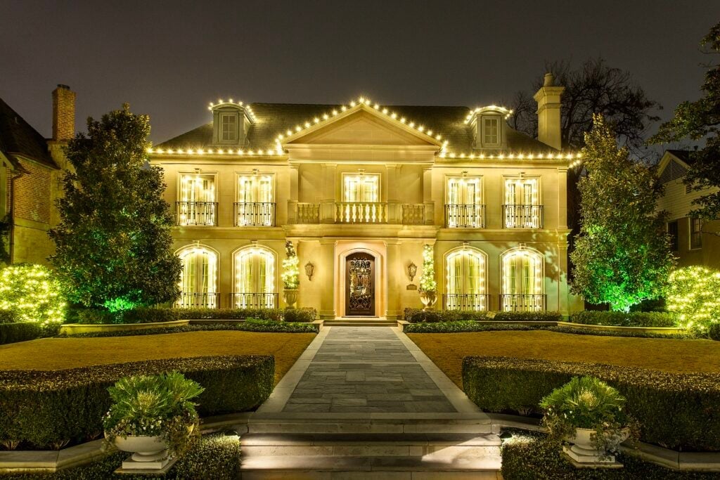 Tile roof edges outlined in warm lights and uplit landscaping.