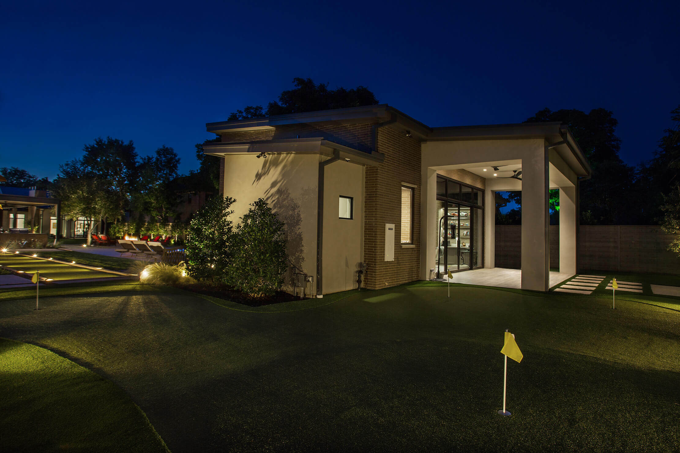 A modern building at night with outdoor landscaping and illuminated putting greens featuring yellow flags.