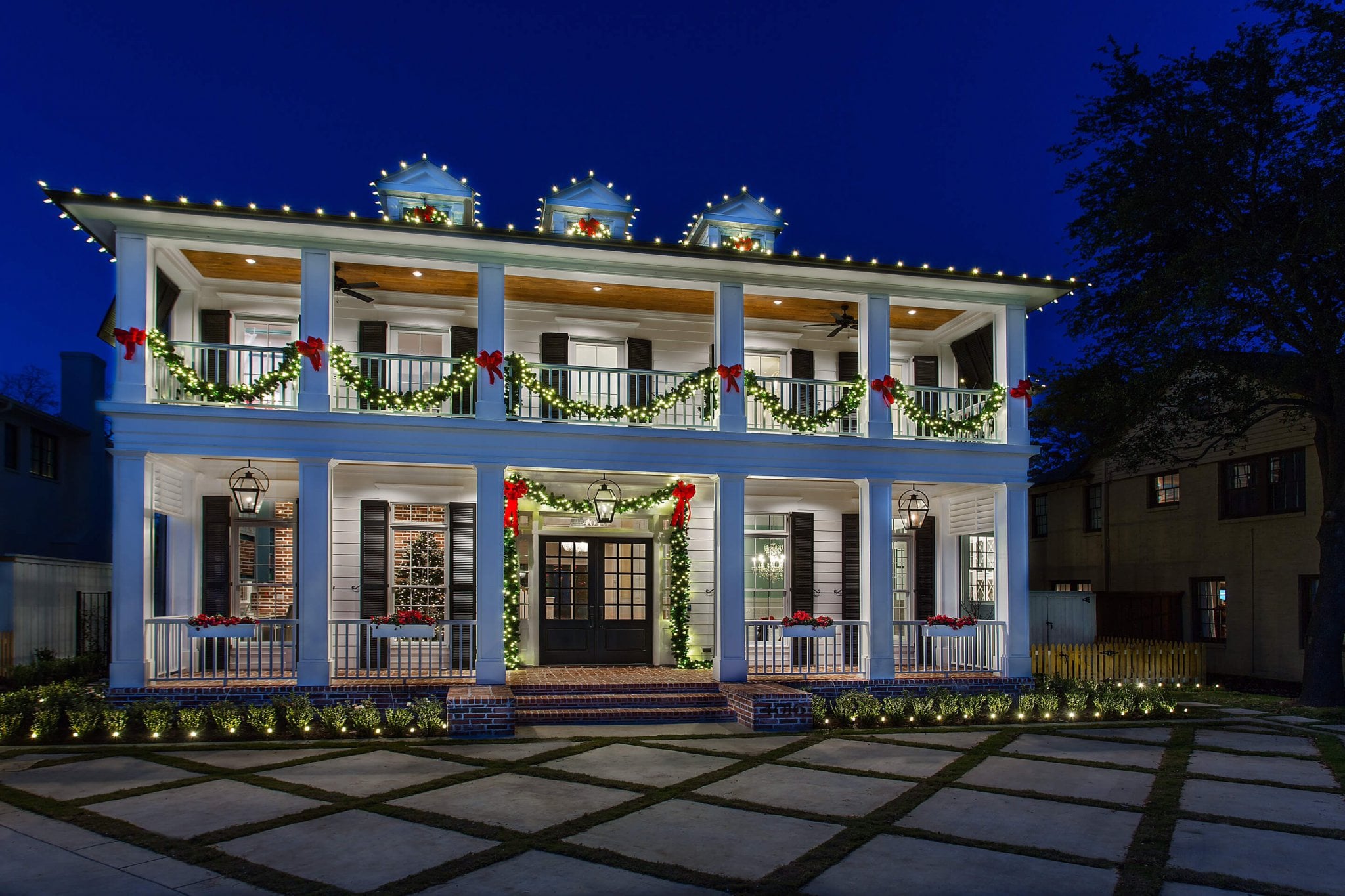 White two-story colonial with garland and red bows along the balcony railings.
