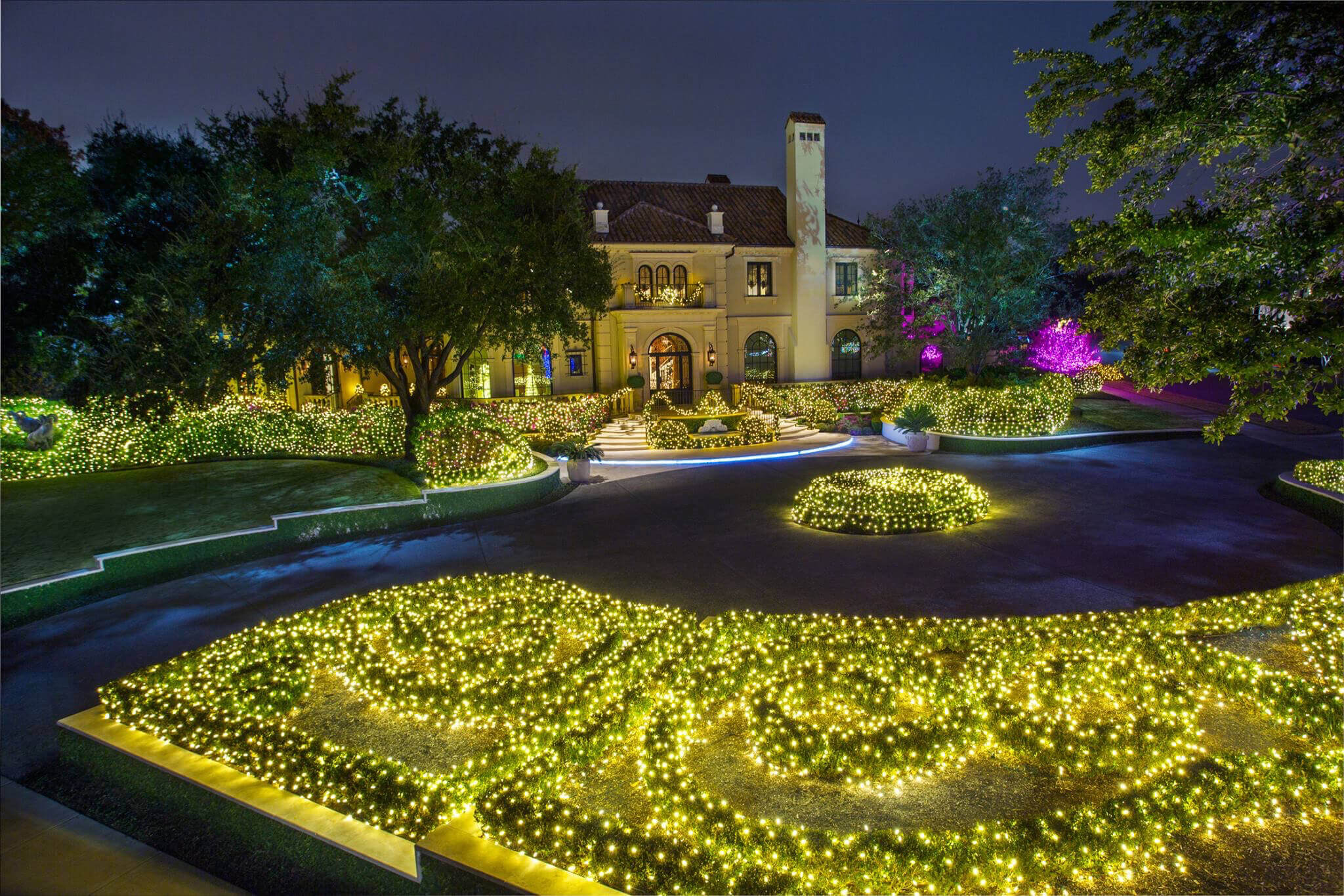 Front lawn covered in yellow-green lights with a lit home in the background.