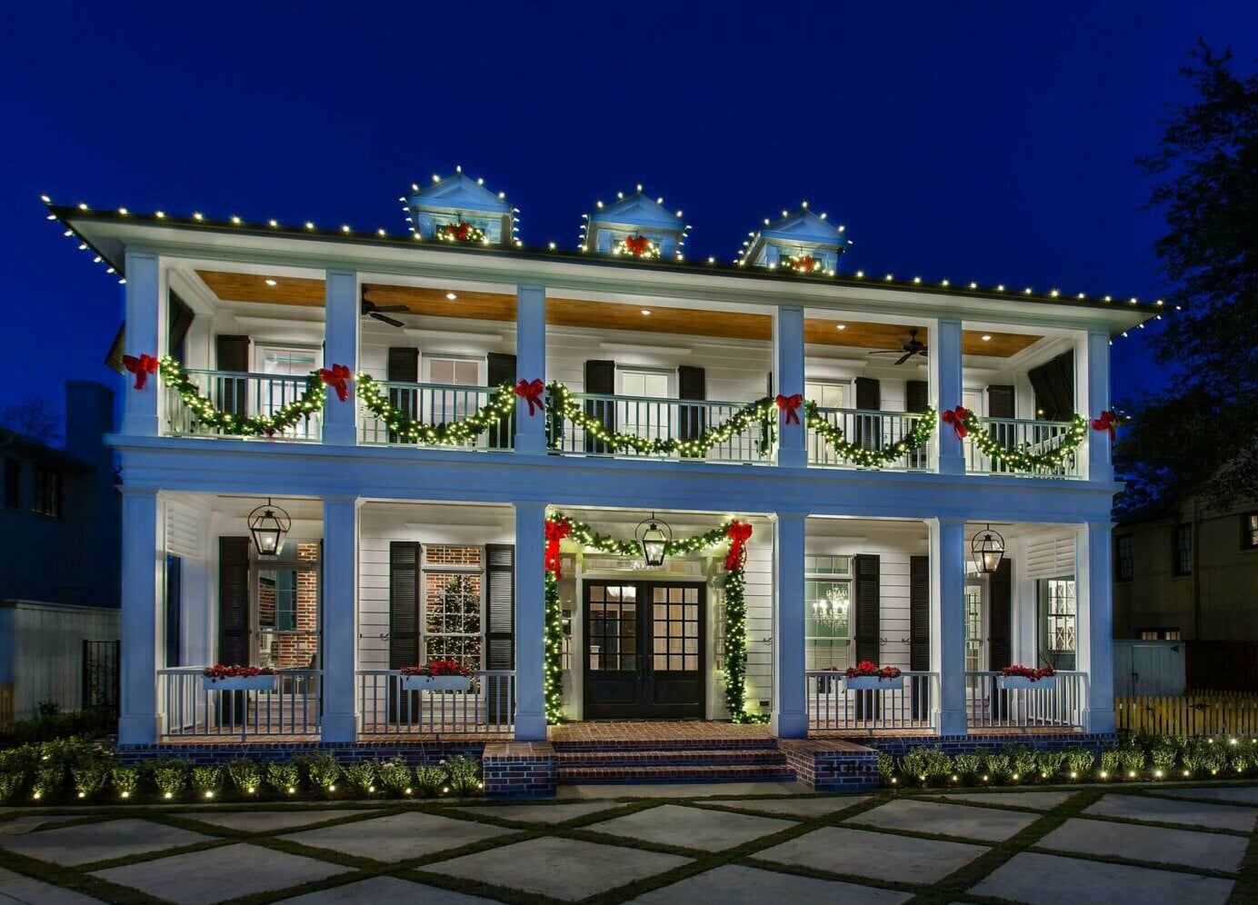 A beautifully decorated two-story house at night, adorned with Christmas lights and garlands, with a charming front porch.