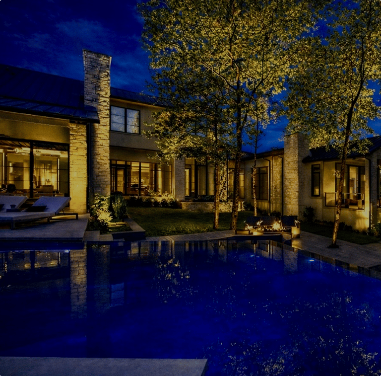 Modern home at night with warm landscape lighting reflected in a lit pool
