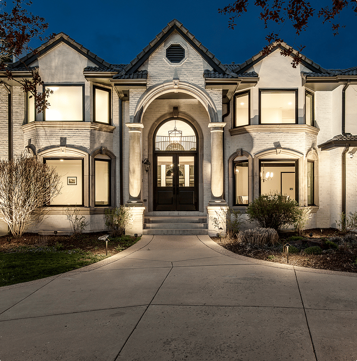 Two-story stone home lit with warm architectural and landscape lighting at night