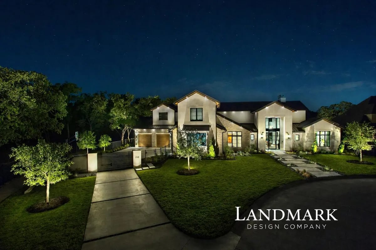 Modern farmhouse at night with uplit trees and a lit front walkway