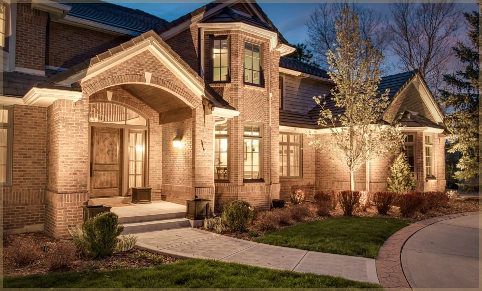 Brick home at dusk with landscape lighting on the entry, trees and walkway